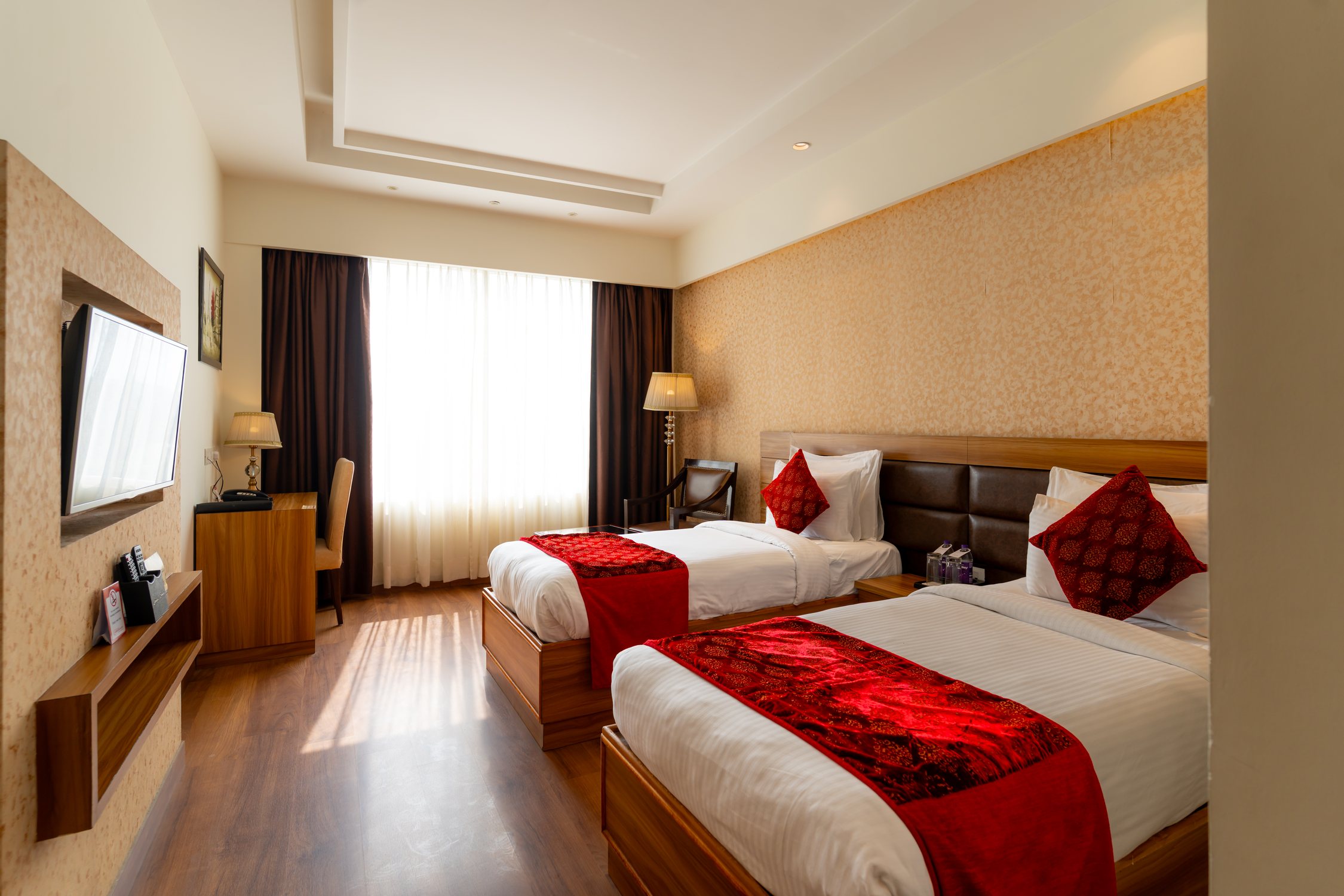 A twin room in daylight, two beds made up with red runners